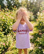 Child wearing a shirt that says 'MAMA'S BIGGEST FAN' in a garden setting