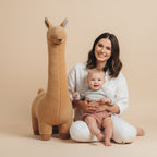 Woman and child sitting on a large brown plush toy resembling a deer in a bright room.