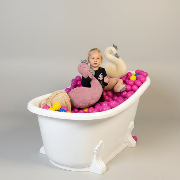 Child playing with plush swans and colorful balls in a ball pit against a black and white striped wall.
