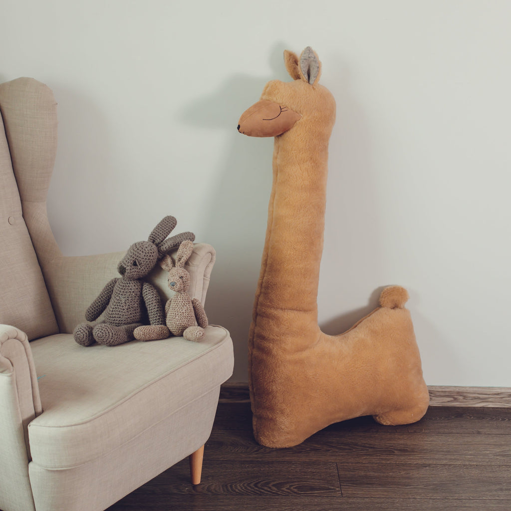 Beige armchair with stuffed animals and a large plush llama toy against a white wall.
