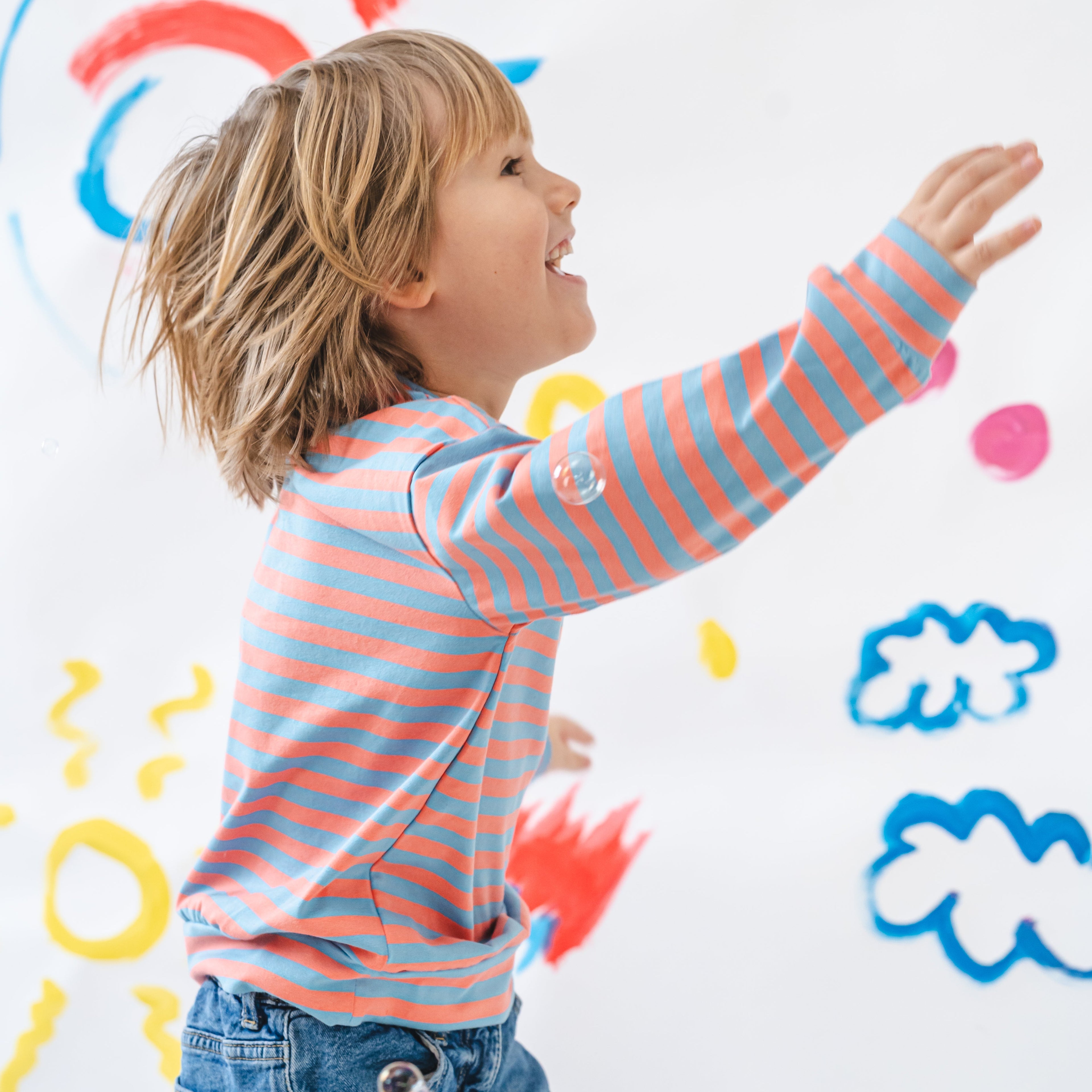 Child in a striped shirt standing in front of a colorful wall with abstract shapes