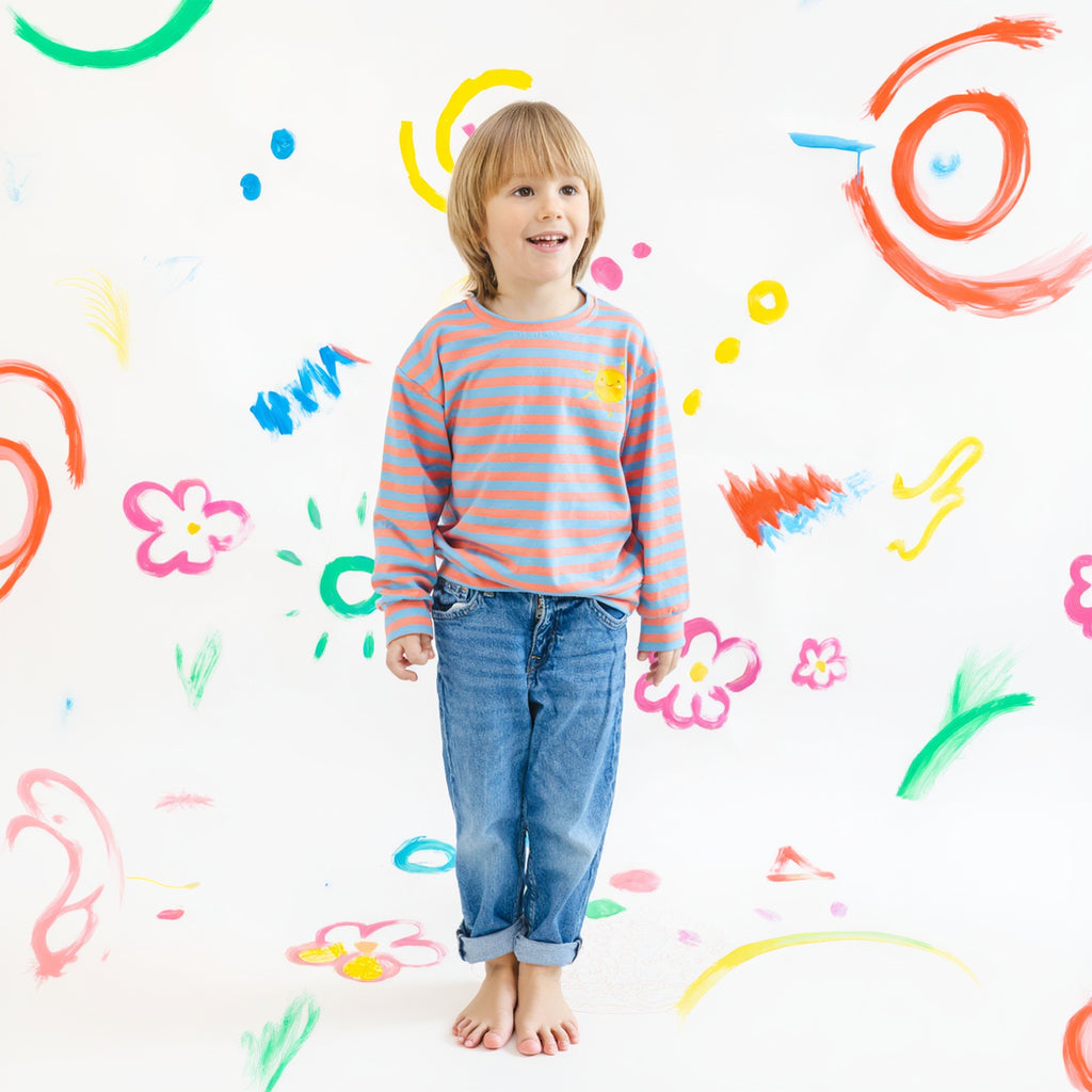 Child wearing a striped shirt and jeans standing against a colorful, child-like drawing background.