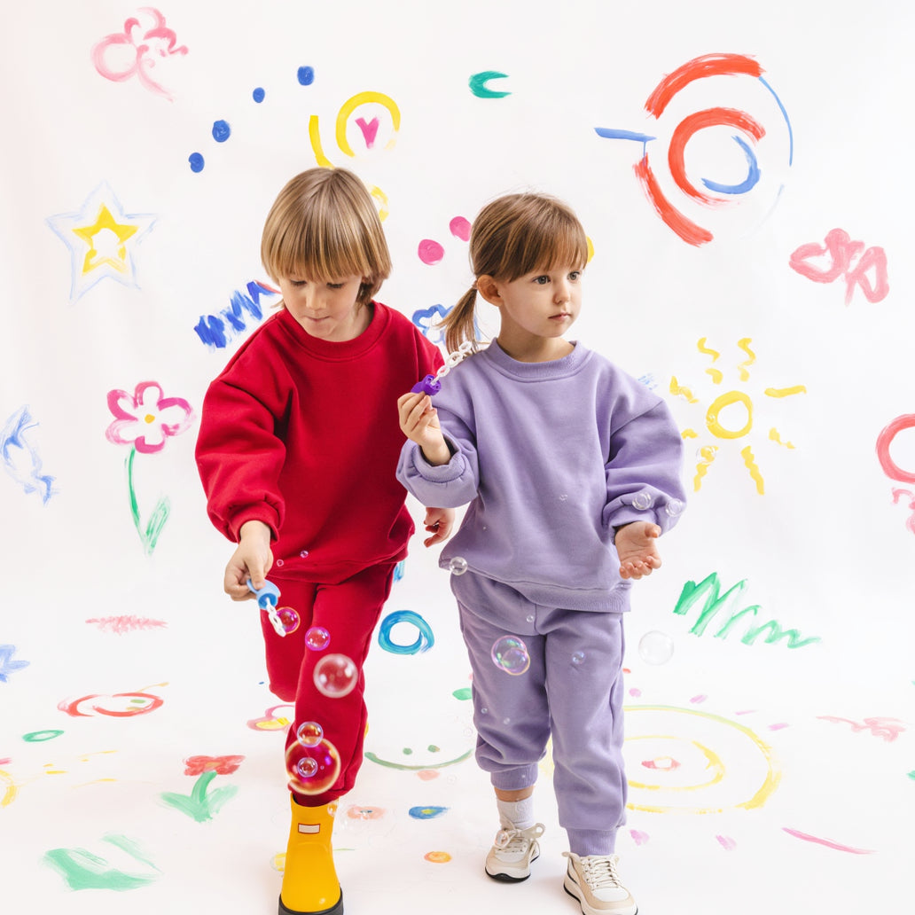 Two children in colorful outfits standing on a white background with playful designs.