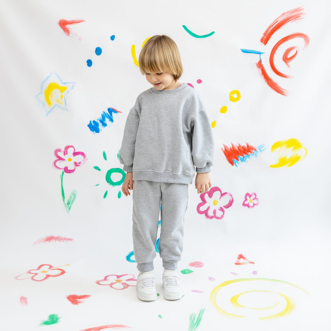 Child wearing a gray helloshams set standing against a colorful, child-drawn background