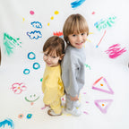Two children standing back-to-back against a colorful, child-drawn background