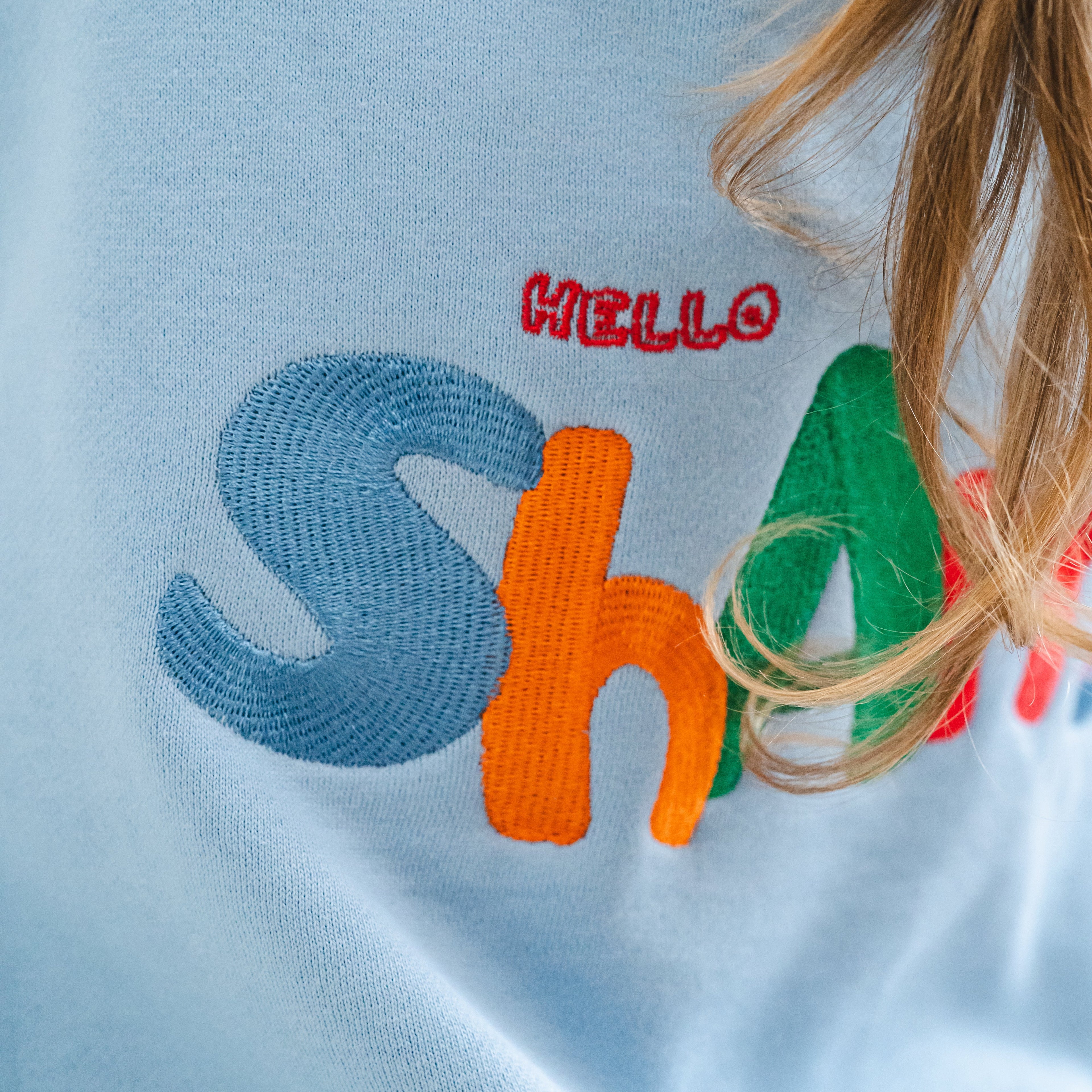 Light blue shirt with colorful text 'HELLO SHAms' on a plain background
