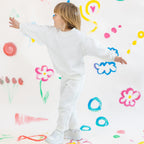 Child in a white outfit standing against a wall with colorful drawings