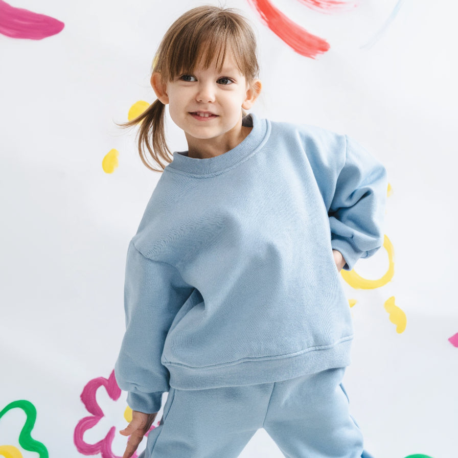 Child wearing a light blue outfit against a colorful abstract background