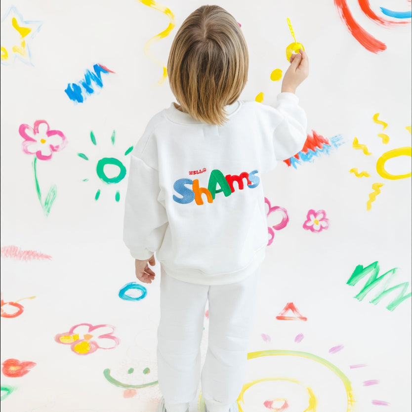 Child drawing on a wall with colorful marks wearing a white shirt with colorful text.