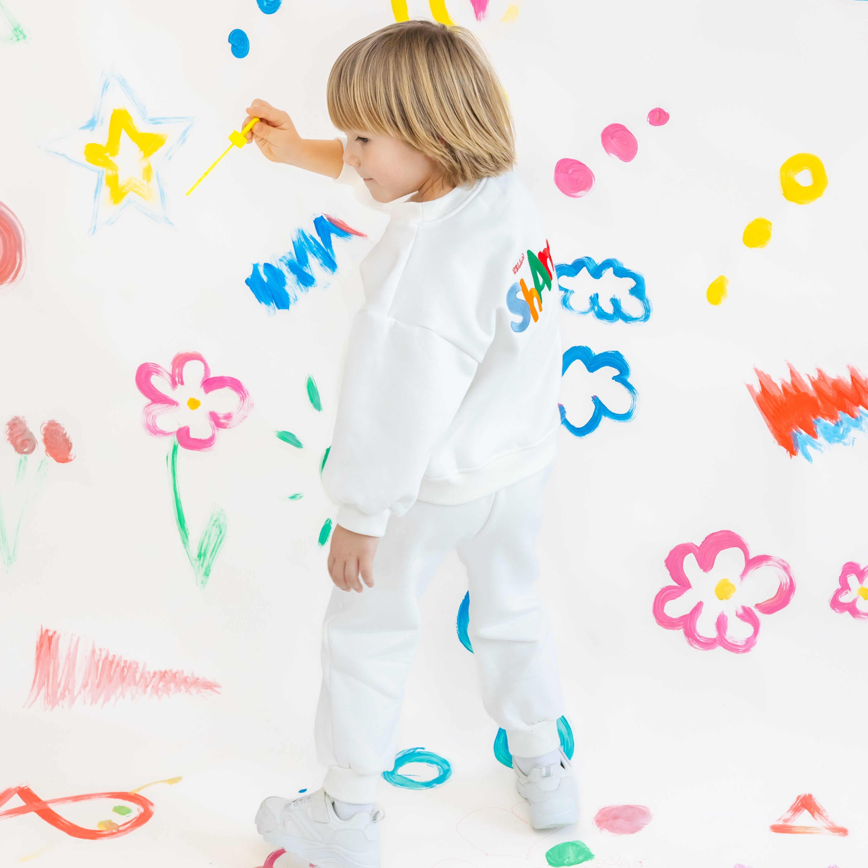 Child in a white sweatset with colorful paint splashes on a white wall