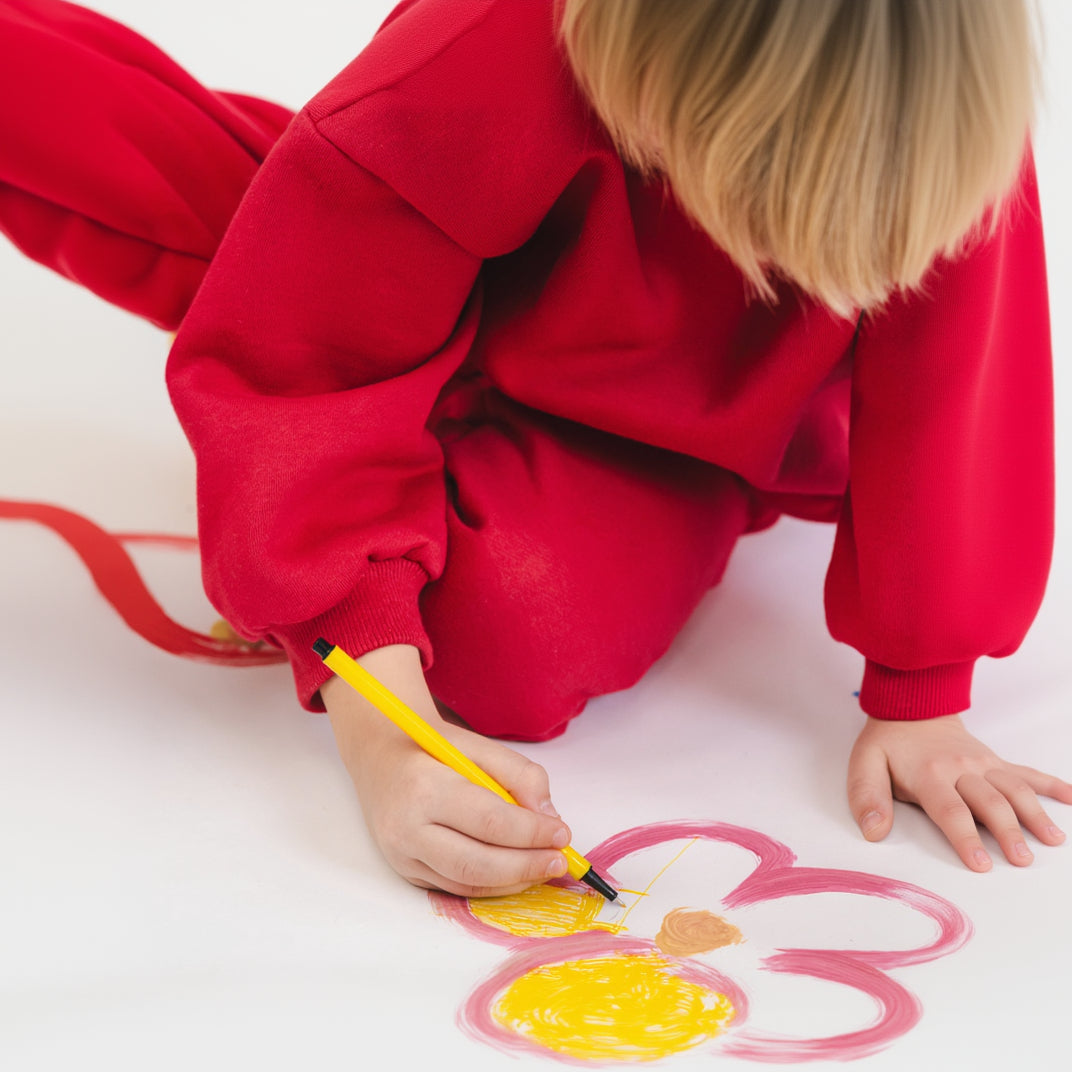 Child in red outfit coloring a flower drawing on a white surface