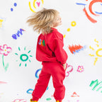 Child in a red outfit standing on a white background with colorful hand drawings.
