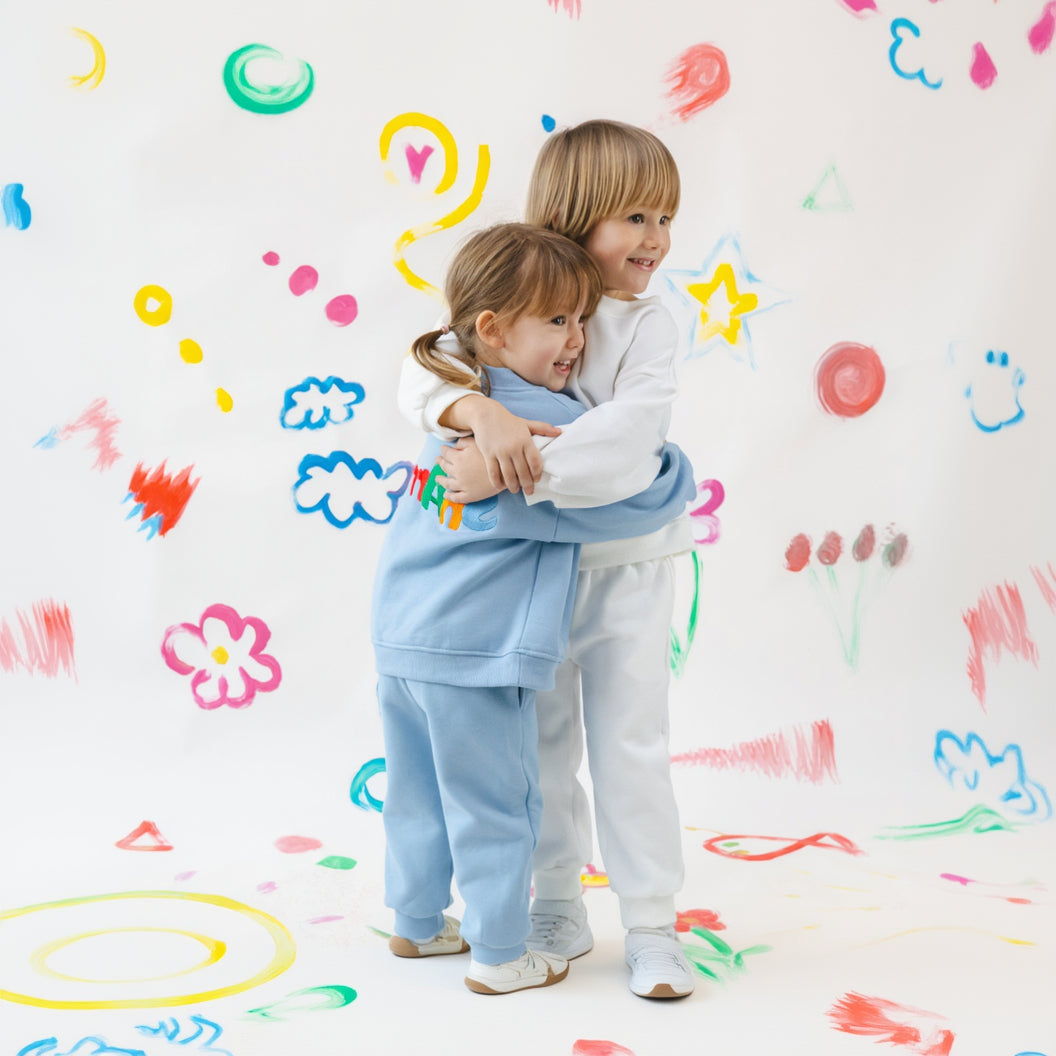 Two children hugging on a white wall with colorful drawings.