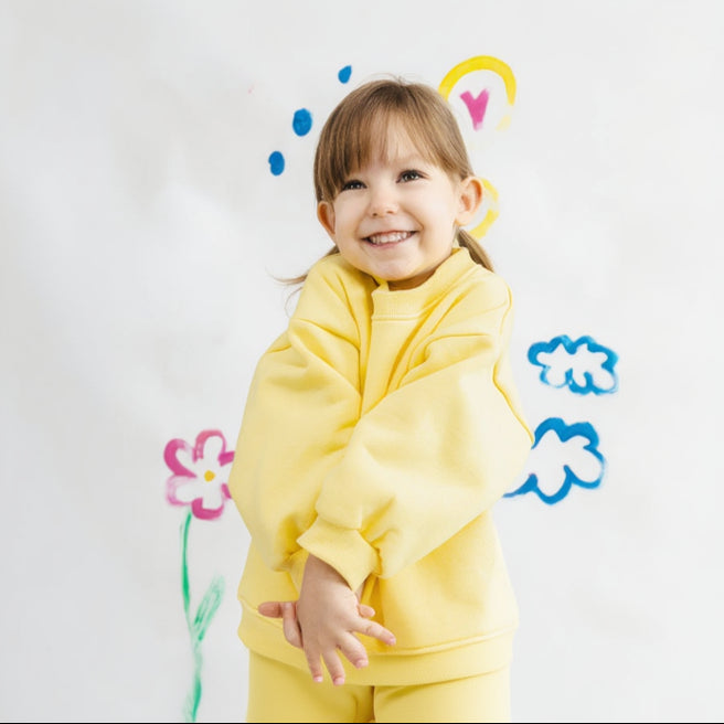 a happy Child wearing a yellow hoodie with colorful drawings on a white background